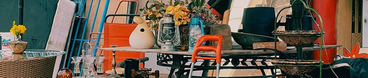 Table at a car boto sale, with a mixture of items including lanterns, a yellow flower in a pot, an orange campring chair