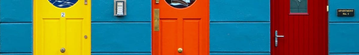 A row of three front doors, yellow, orange, and red, set in a blue wall.